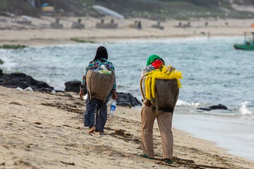 Free Two fishermen carrying woven baskets walk along a tranquil coast, capturing daily life by the sea. Stock Photo