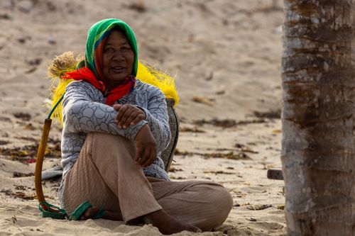 Free A woman with a colorful headscarf sits in relaxed pose on a sandy beach. Stock Photo