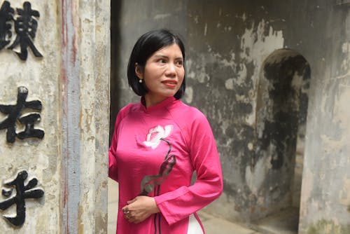A woman in a pink shirt standing next to a wall with chinese writing
