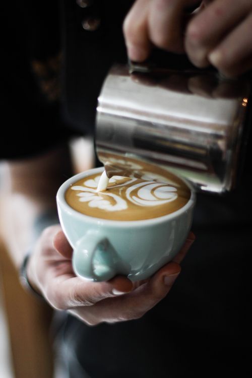 Free Close-up of a barista making intricate latte art in a cozy coffee shop setting. Stock Photo