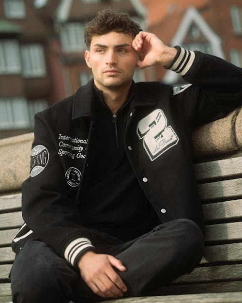 A young man sitting on a bench wearing a jacket