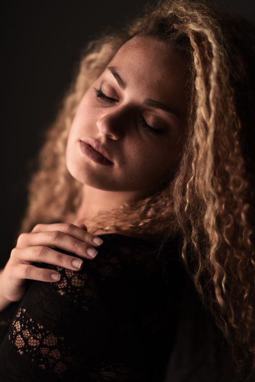 Free Elegant portrait of a young woman with curly blonde hair in black lace, eyes closed, serene expression. Stock Photo
