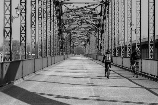 Two cyclists ride across an iconic Hamburg bridge in a black and white urban setting.