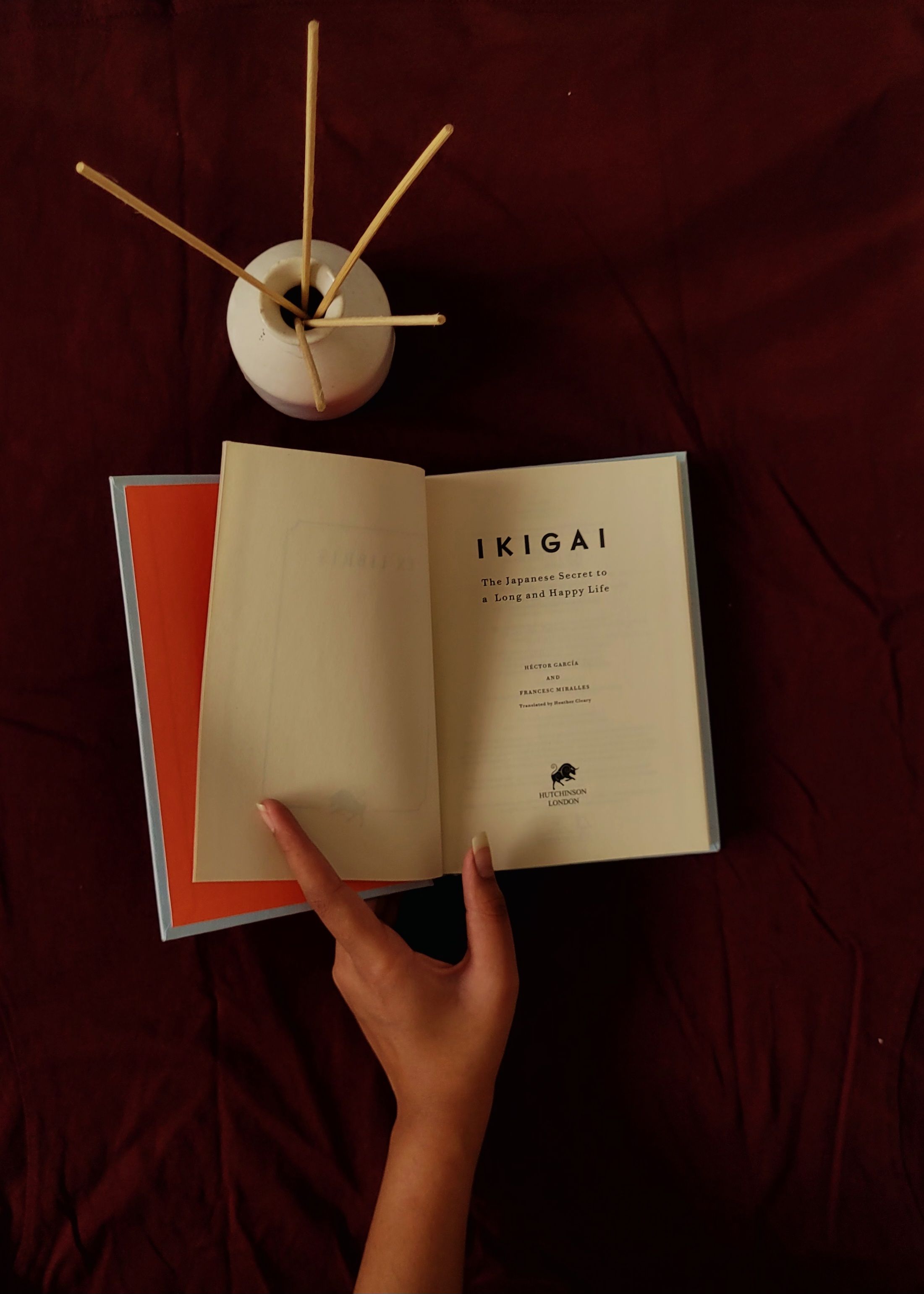 A calming scene of a hand holding the book 'Ikigai' on a table with incense sticks, promoting relaxation.