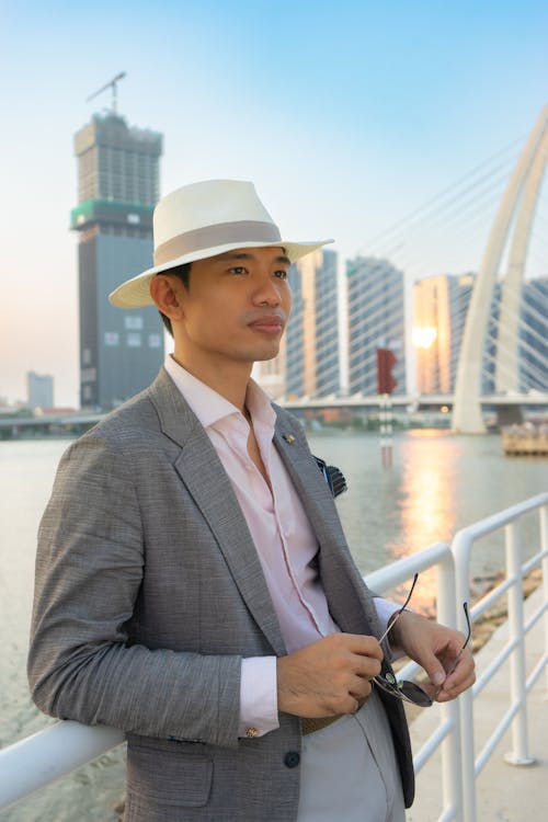 A man in a suit and hat standing near a river