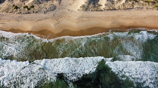A stunning aerial perspective of a sandy beach with gentle waves and clear ocean water.