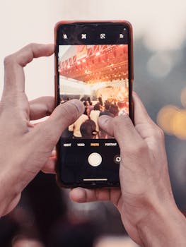 A close-up shot of hands holding a phone capturing a live music concert.