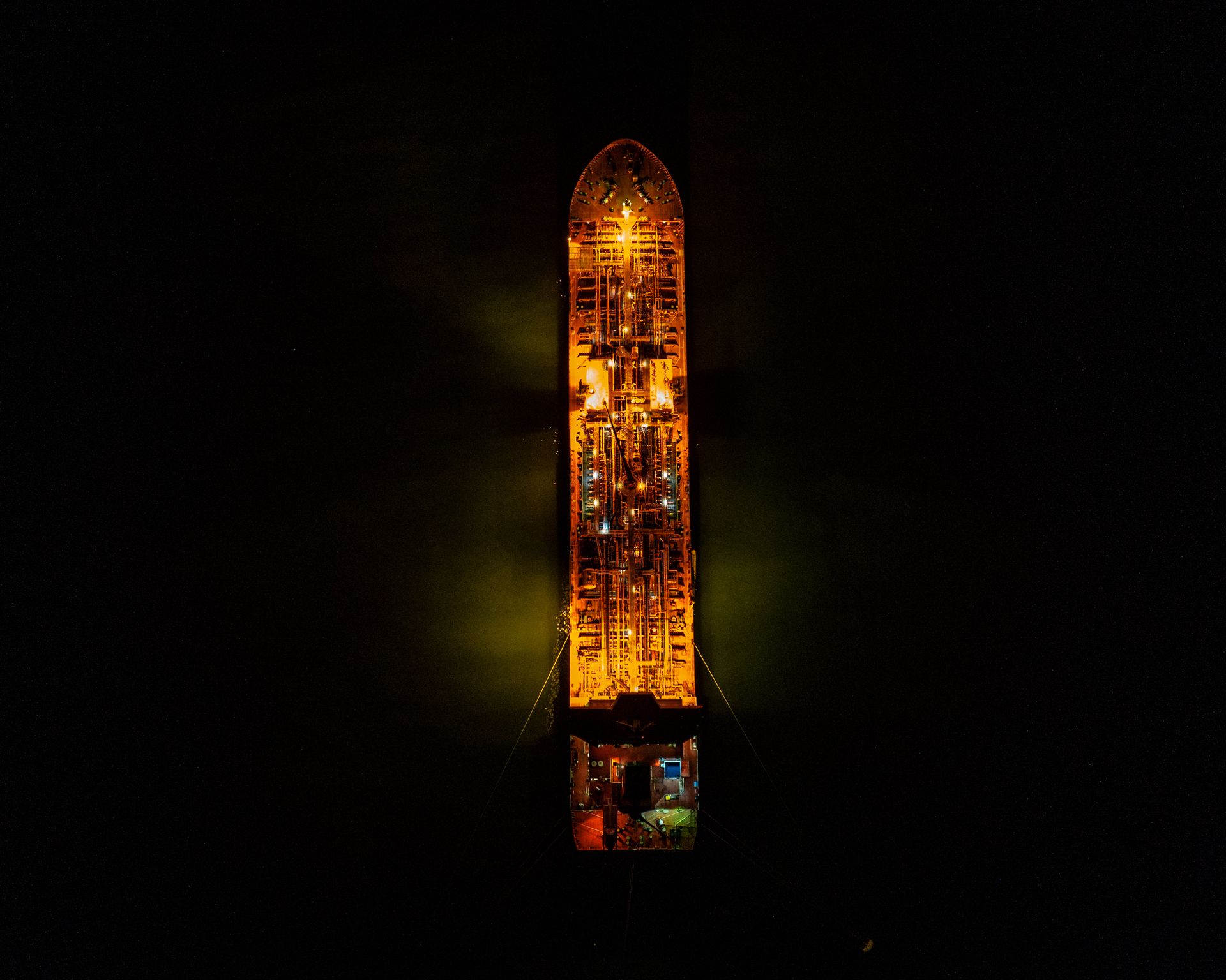 Top-down aerial shot of an illuminated cargo ship at night in the sea.