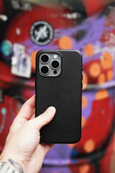 Close-up of a smartphone held by a hand against a vibrant graffiti wall.