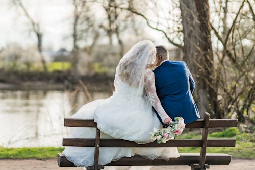 A bride and groom sitting on a bench by the water
