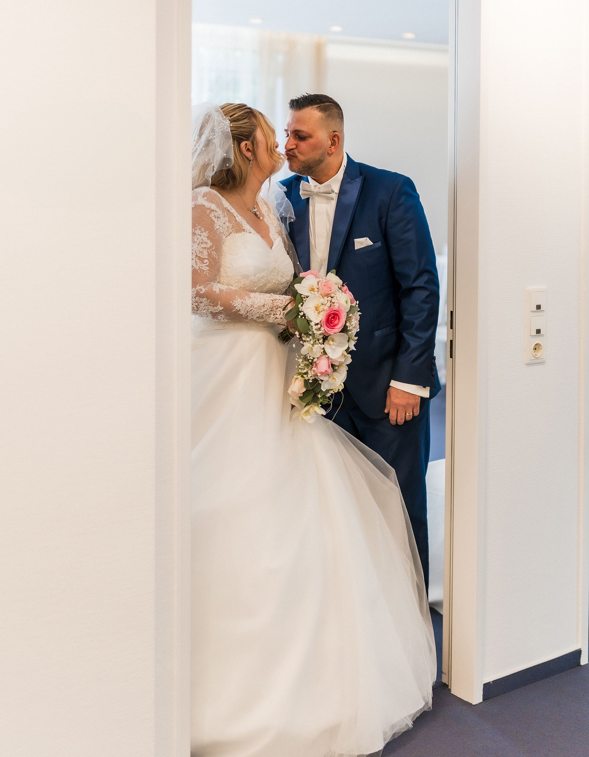 Bride and groom sharing a romantic moment on their wedding day, dressed elegantly indoors.