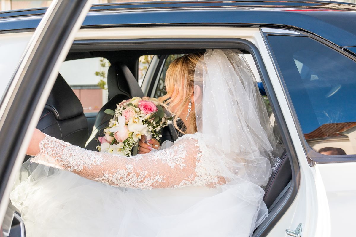 Bride in a lace wedding dress holding a bouquet inside a car