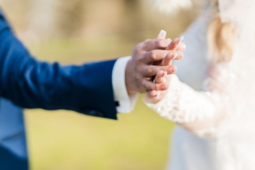 Close-up of a bride and groom holding hands on their wedding day, symbolizing love and commitment.