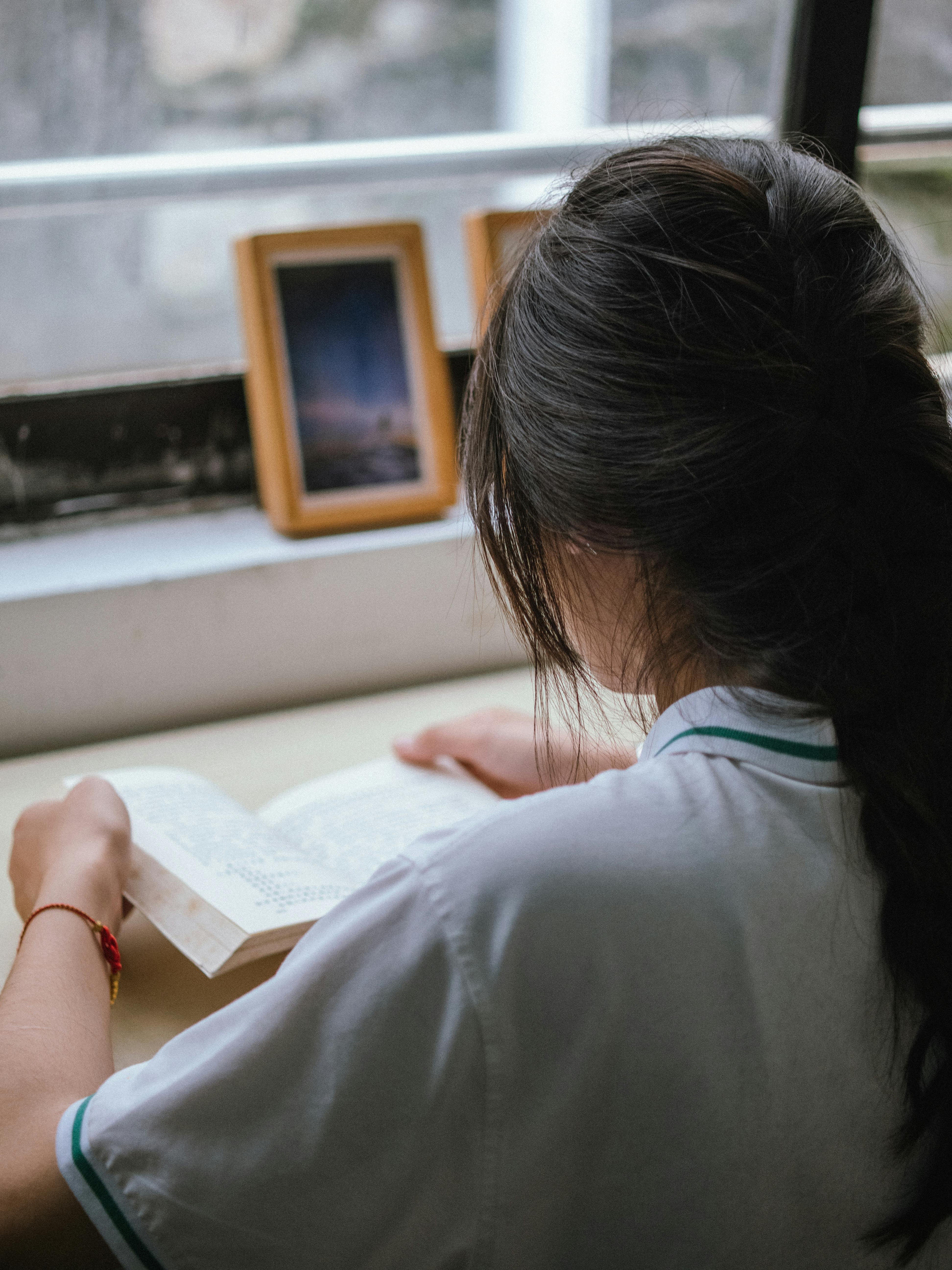 A woman reads a book by the window, enjoying peaceful natural light in a cozy setting.