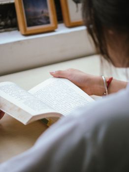A woman sits by the window reading a book, creating a cozy indoor atmosphere.