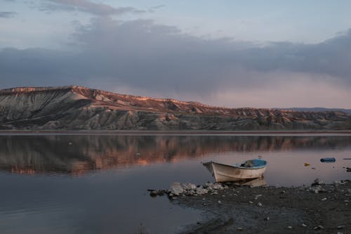 A Boat Moored on the Shore of a Calm Body of Water with Hills in the Background 