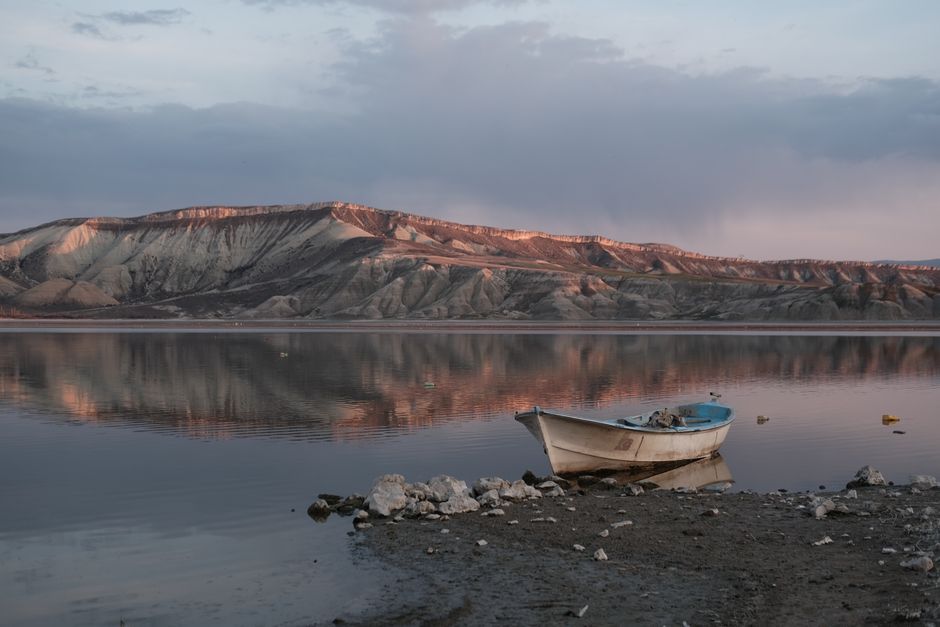 Serene scene of a boat on Nallıhan Lake at sunrise with stunning mountain reflections.