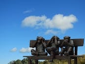 雕塑描绘了三只聪明的猴子坐在户外蓝天下的长凳上