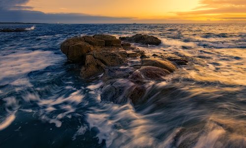 Free Beautiful sunset over a rocky ocean shore, capturing vivid colors and dynamic waves. Stock Photo