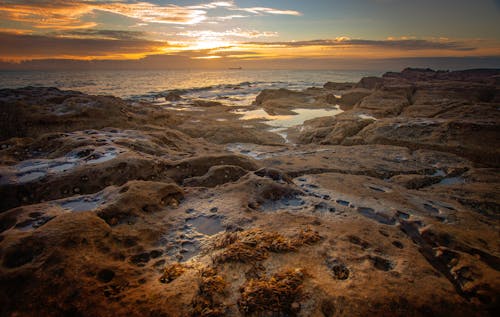 A sunset over the ocean with rocks and water