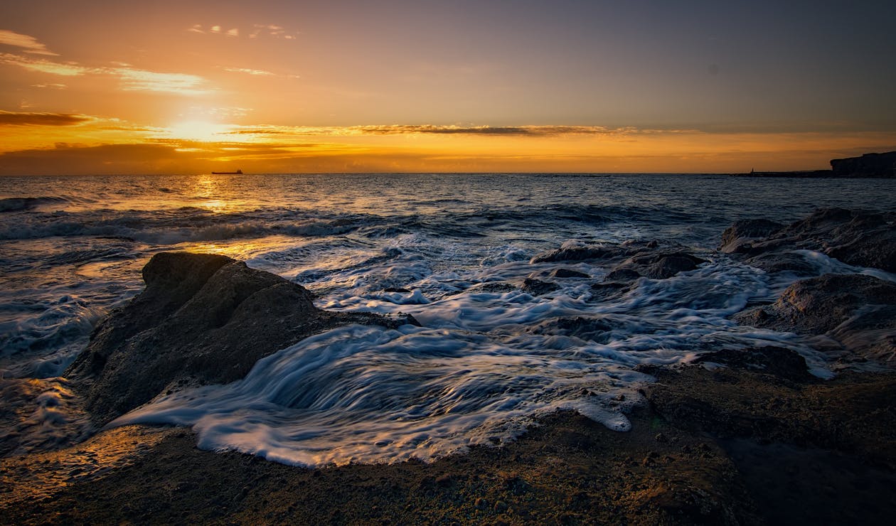 A sunset over the ocean with rocks and water