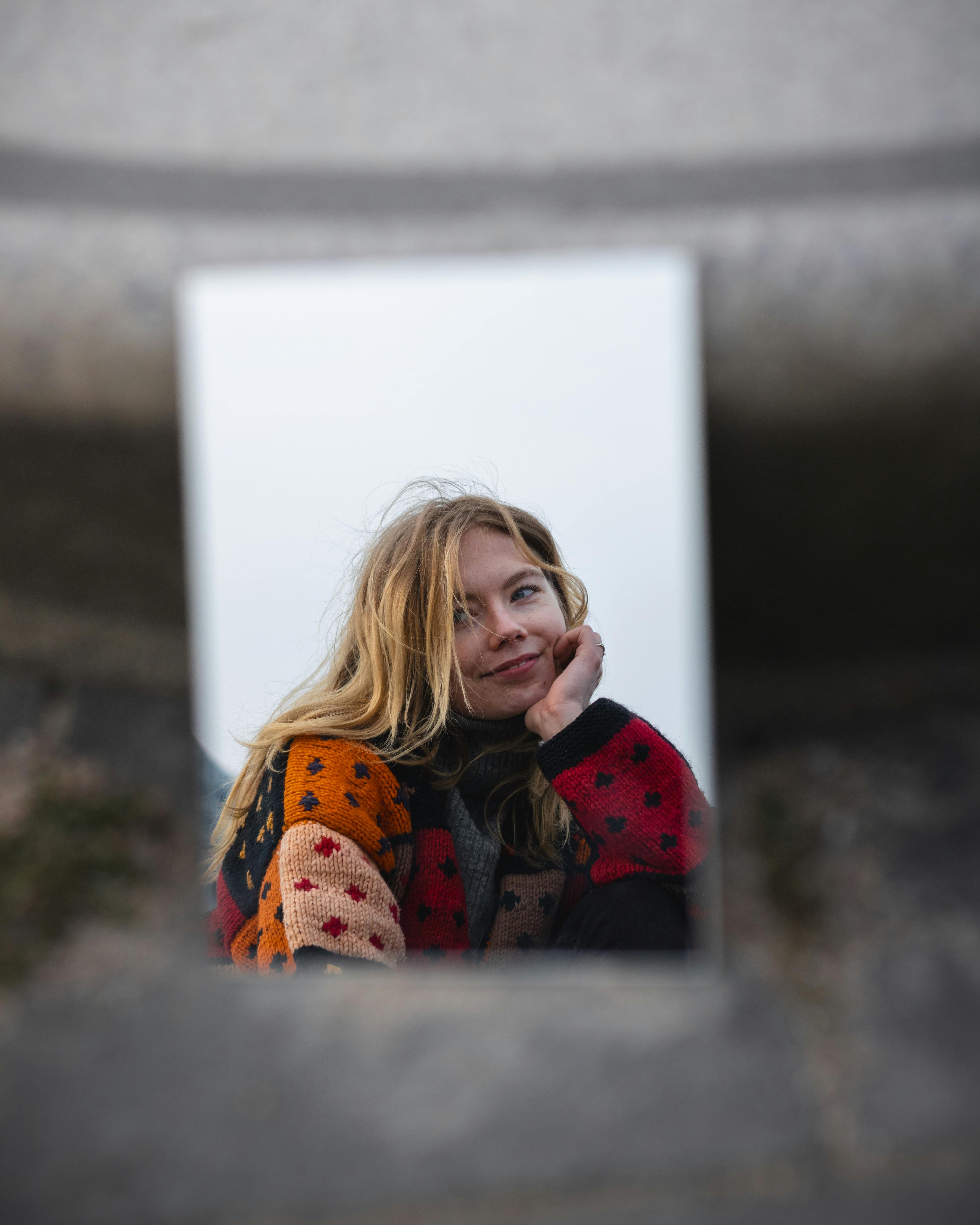 A captivating portrait of a young woman reflected in a mirror outdoors, showcasing serene beauty.