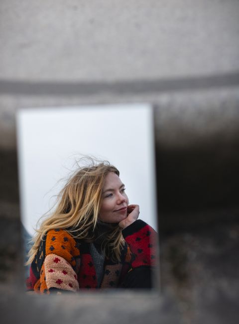 A woman smiling in a mirror reflection set in urban Hamburg, captured in fall. Vibrant and artistic.
