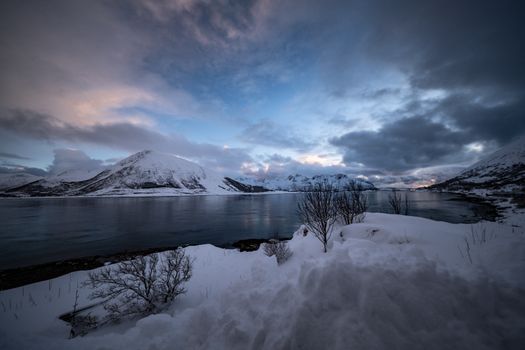 Snow-covered mountains and tranquil lake at dusk, showcasing winter's serene beauty.