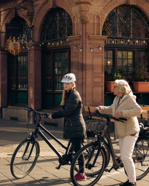 Free Two women with bicycles stand outside a cafe in an urban setting. One wears a helmet. Stock Photo