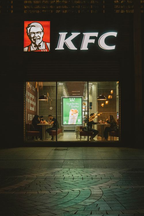 Free Nighttime view of a KFC storefront with diners visible through the glass facade. Stock Photo