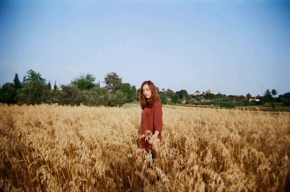 A young woman stands in a serene wheat field surrounded by nature at dusk, embodying tranquility.