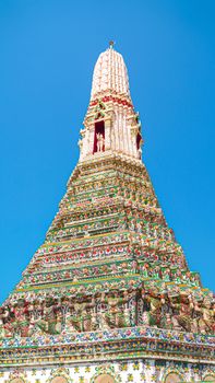Detailed view of Wat Arun's ornate spire in Bangkok, Thailand, against a clear blue sky.