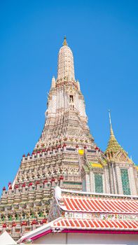 Colorful facade of Wat Arun temple against a clear blue sky in Bangkok, showcasing traditional Thai architecture.