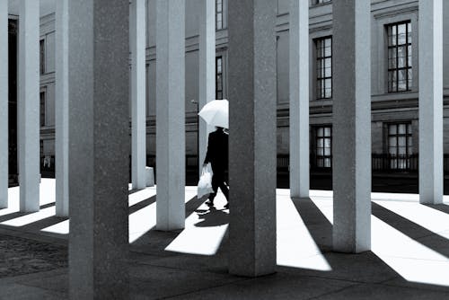 Person with Umbrella Walking among Building Pillars