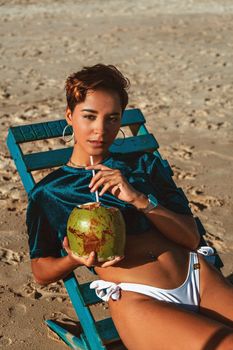 Young woman on a sunbed enjoying a fresh coconut drink at the beach on a sunny day.
