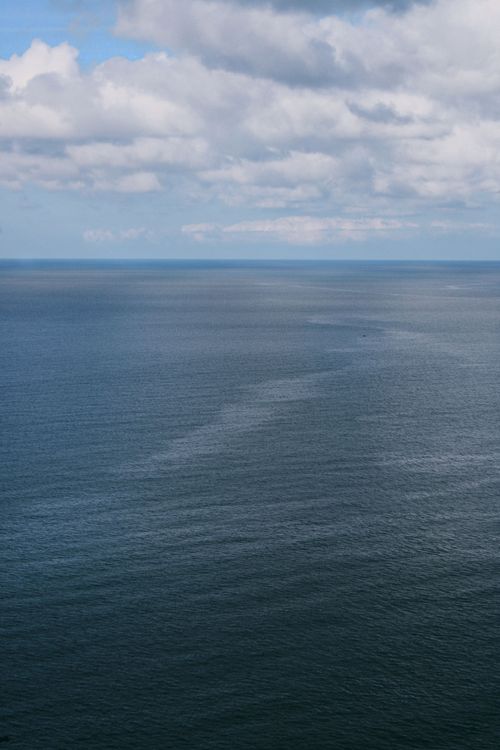Free Serene aerial view of the vast ocean with scattered clouds in the sky above. Stock Photo
