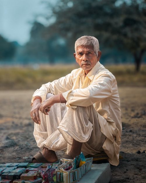 Free Elderly man in rural India sitting on the ground in traditional clothing, thoughtful expression. Stock Photo