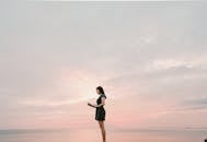 日落时分，一名女子穿着连衣裙，在宁静的海边读书