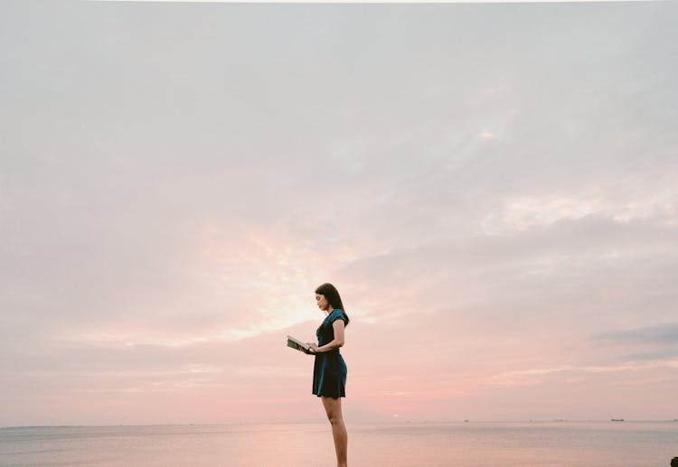 Woman Wearing Black Dress Standing And Reading Book