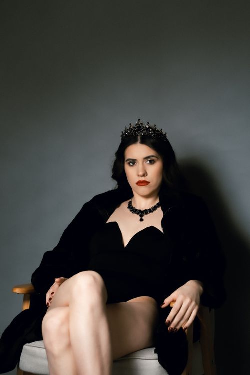 Free A sophisticated portrait of a woman in black attire, tiara, and elegant jewelry seated on an armchair. Stock Photo