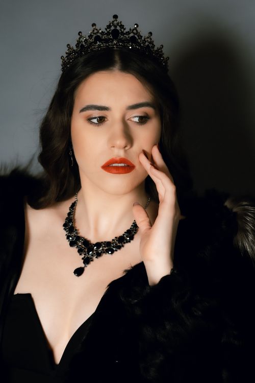 Free Sophisticated portrait of a woman with red lipstick, black crown and necklace, evokes elegance. Stock Photo