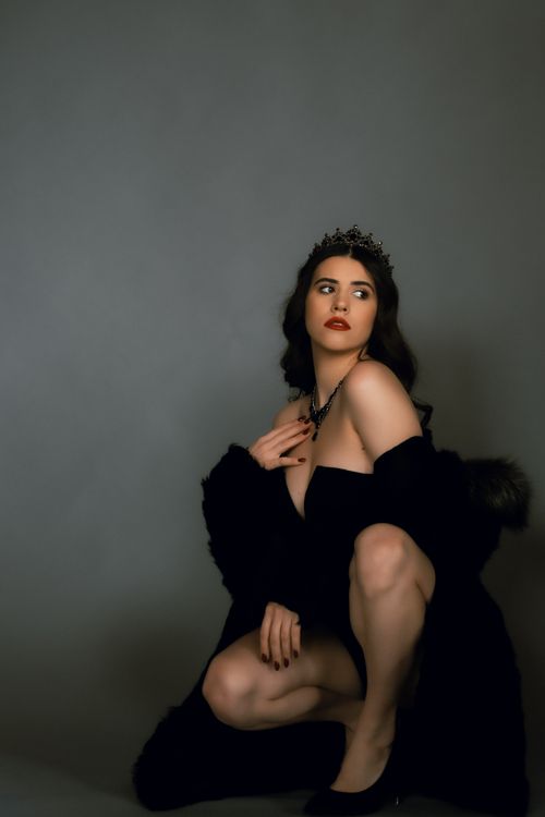 Free Model wearing a crown and black coat posing on a gray background, exuding elegance and sophistication. Stock Photo