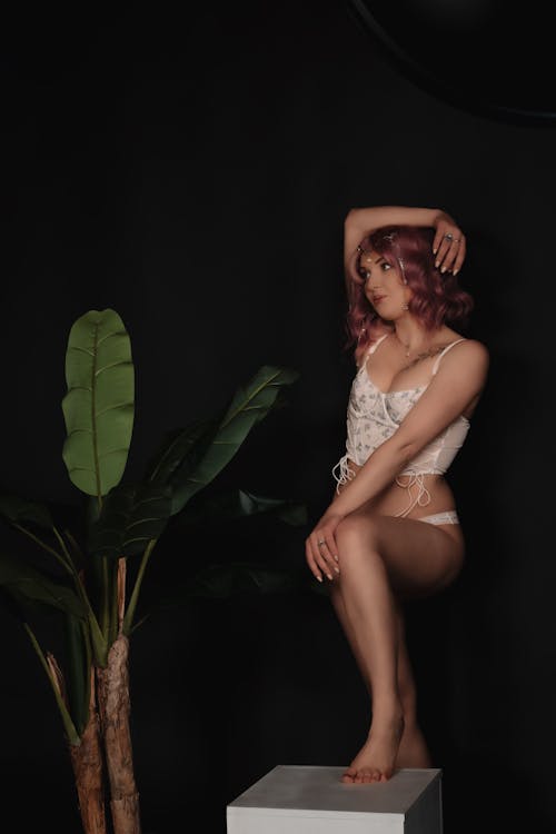 A woman in underwear sitting on a box with a plant