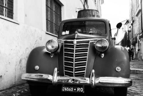 Black and white photo of an old car on a cobblestone street
