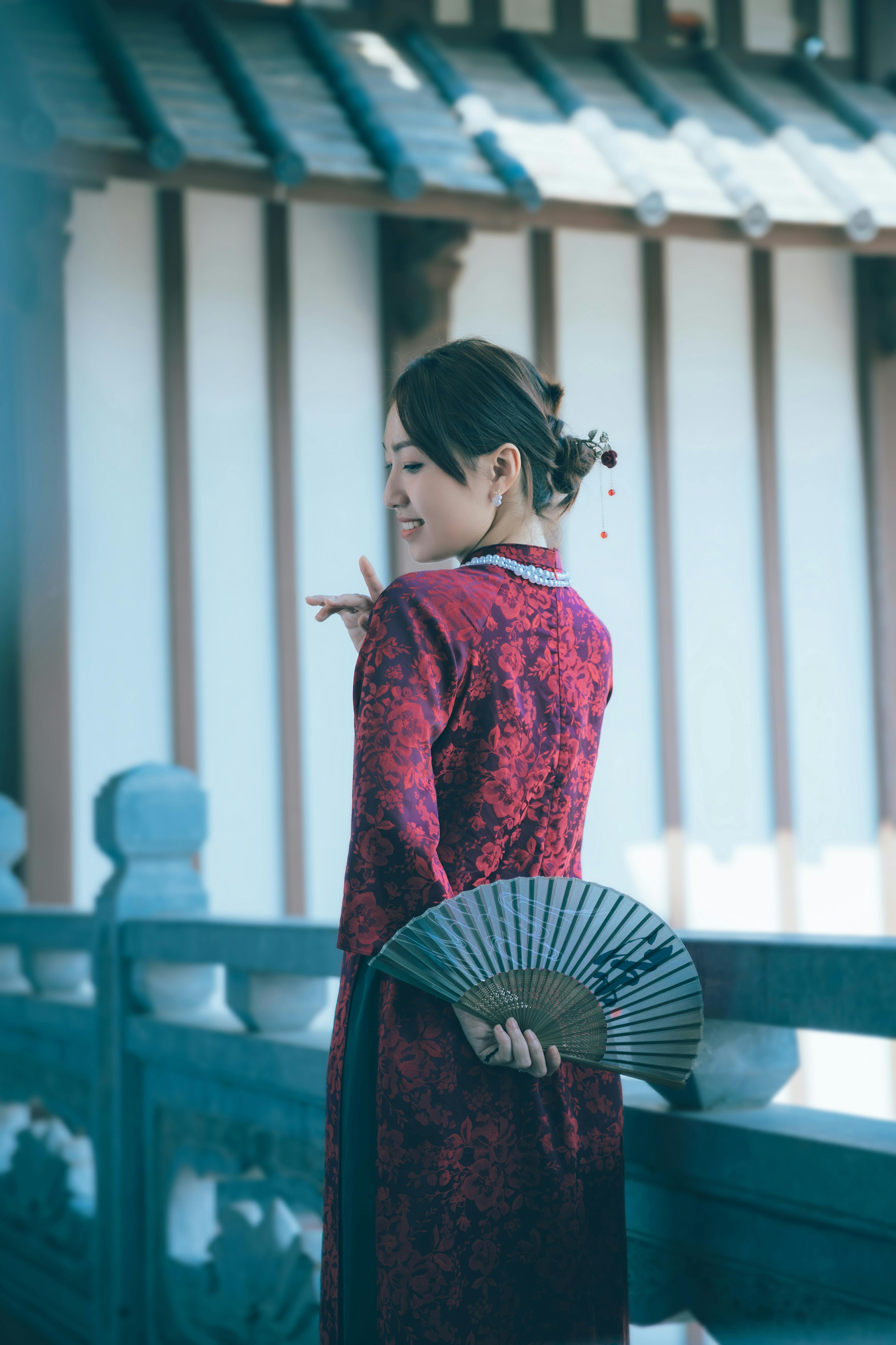 A stylish woman in a red dress holding a folding fan in traditional setting.