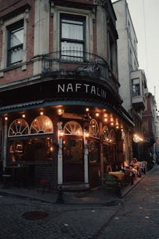 Warmly-lit cafe on a cobblestone street in Istanbul, Türkiye, evoking a nostalgic and moody atmosphere.