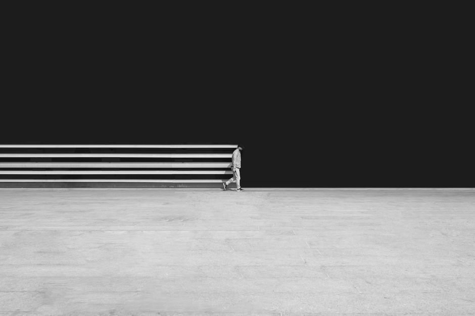 Black and white photo of a man walking on pavement in Tehran, showcasing minimalism and urban solitude.