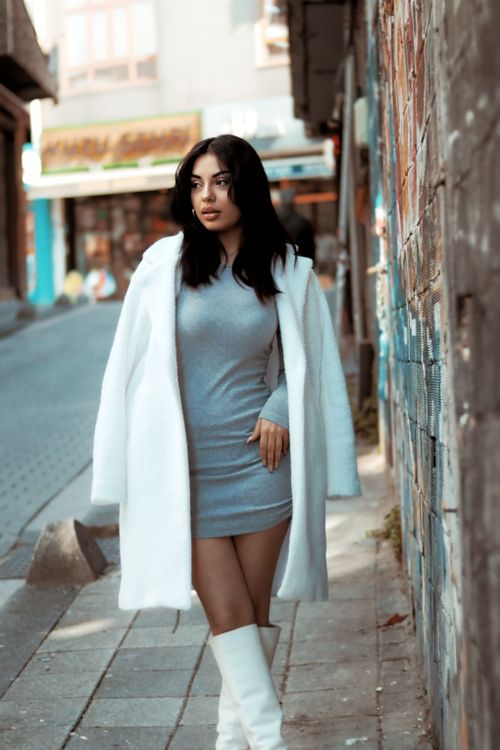 Free Elegant woman in white coat and dress stands confidently on a city street, showcasing urban fashion. Stock Photo