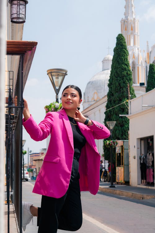 A woman in a pink blazer leaning against a wall