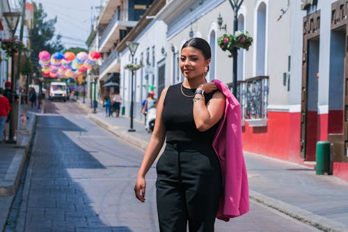 A woman in black pants and pink jacket walking down a city street